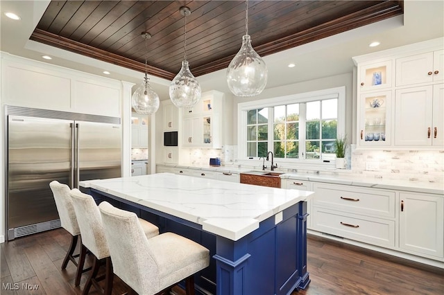 kitchen with hanging light fixtures, a tray ceiling, stainless steel built in fridge, a kitchen island, and white cabinets