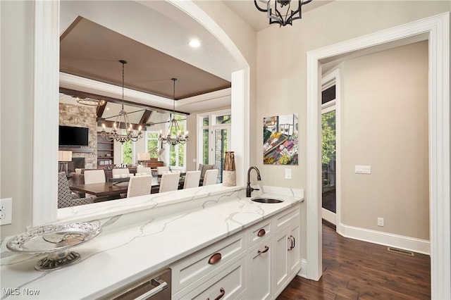 bar with pendant lighting, white cabinetry, sink, a notable chandelier, and light stone counters