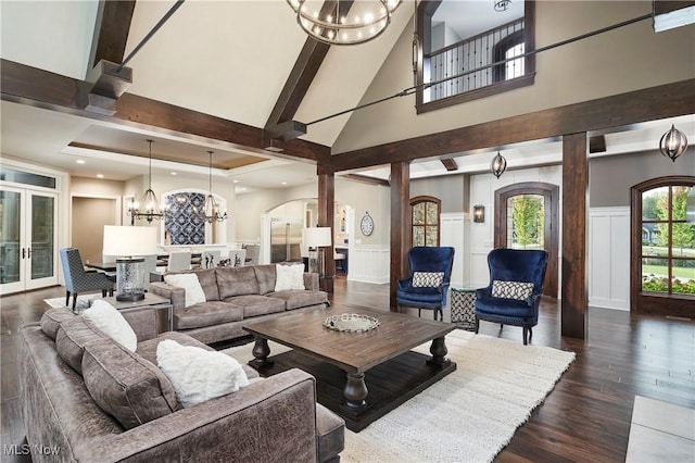 living room featuring a towering ceiling, dark hardwood / wood-style floors, beamed ceiling, a chandelier, and french doors