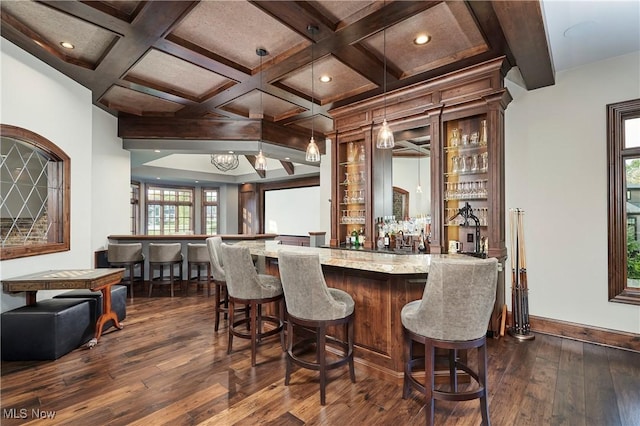 bar with dark wood-type flooring, coffered ceiling, decorative light fixtures, beam ceiling, and light stone countertops