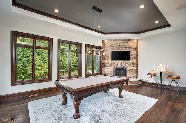 game room featuring dark wood-type flooring, a tray ceiling, a brick fireplace, and a wealth of natural light