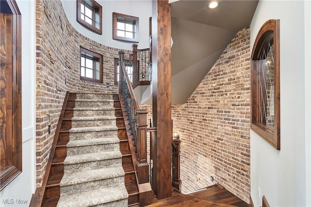 stairs featuring hardwood / wood-style flooring, vaulted ceiling, and brick wall