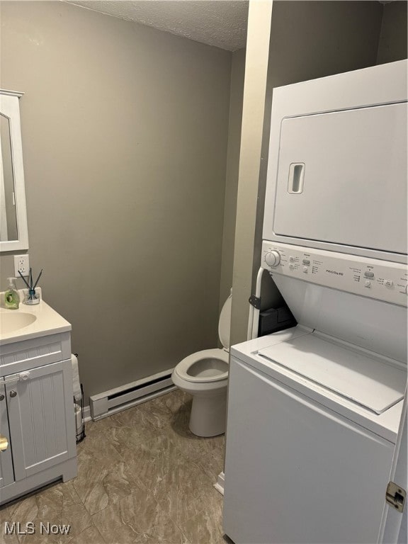 bathroom featuring toilet, stacked washer / dryer, a baseboard heating unit, vanity, and a textured ceiling