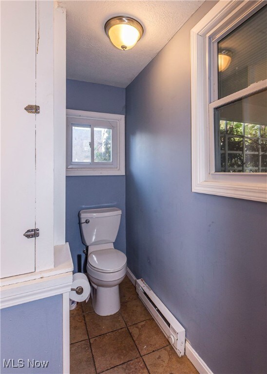 bathroom featuring a baseboard radiator, tile patterned flooring, toilet, and a textured ceiling