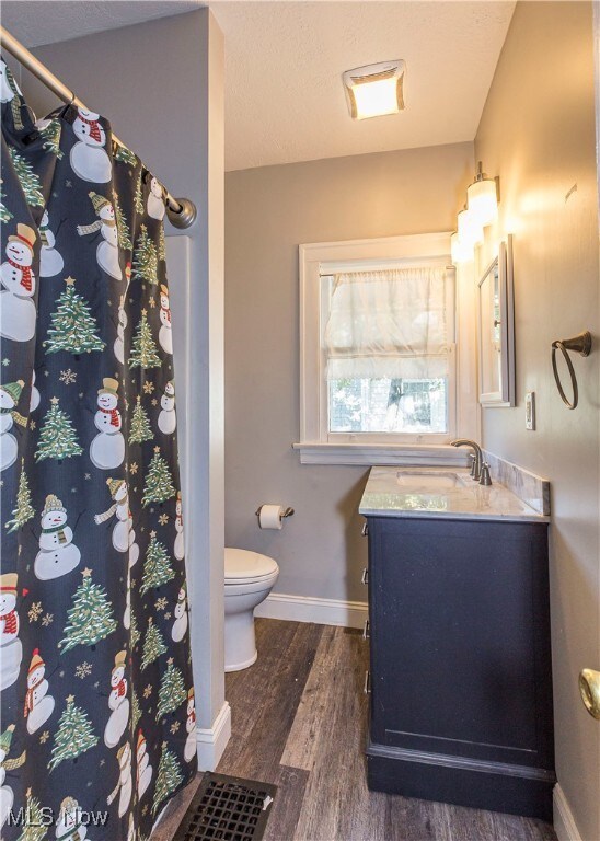 bathroom with wood-type flooring, vanity, walk in shower, and toilet