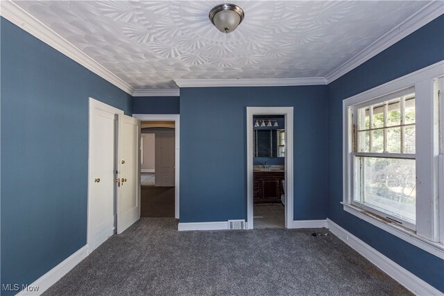 unfurnished bedroom featuring ornamental molding, sink, ensuite bath, and dark colored carpet