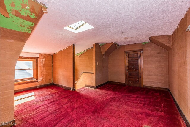 additional living space with a skylight, dark colored carpet, and a textured ceiling