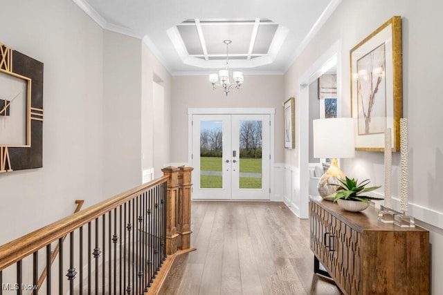 hall featuring light hardwood / wood-style floors, an inviting chandelier, a tray ceiling, crown molding, and french doors