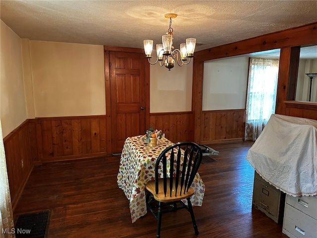 dining space featuring dark wood-type flooring, wood walls, an inviting chandelier, and a textured ceiling