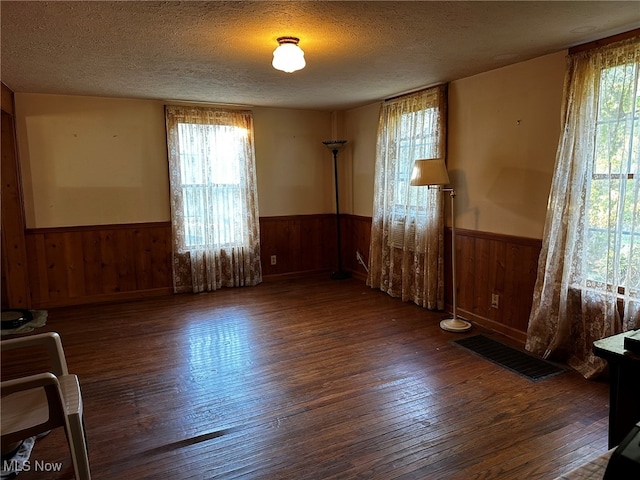 spare room featuring a healthy amount of sunlight, wooden walls, dark wood-type flooring, and a textured ceiling