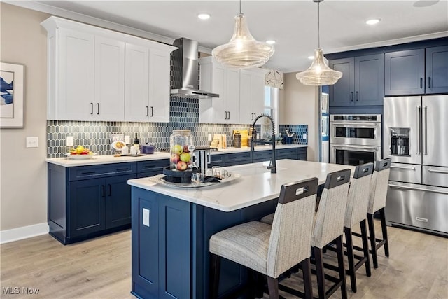 kitchen with wall chimney exhaust hood, light wood finished floors, blue cabinetry, and stainless steel appliances