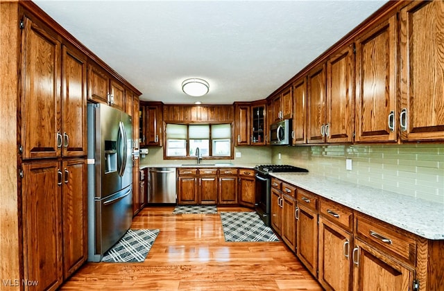 kitchen featuring light stone counters, sink, appliances with stainless steel finishes, light hardwood / wood-style floors, and decorative backsplash