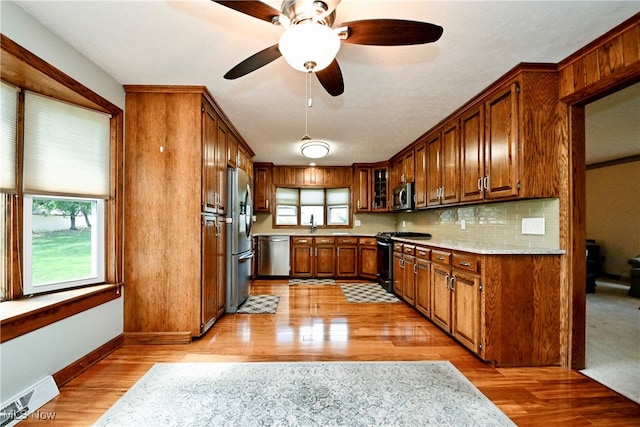 kitchen with light stone counters, ceiling fan, light hardwood / wood-style floors, appliances with stainless steel finishes, and backsplash