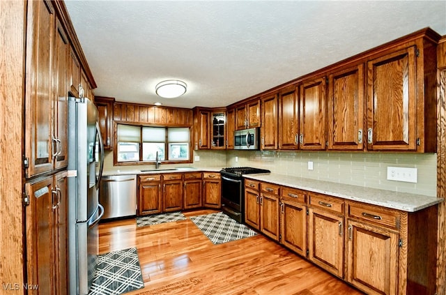 kitchen with light stone countertops, light hardwood / wood-style floors, appliances with stainless steel finishes, and sink