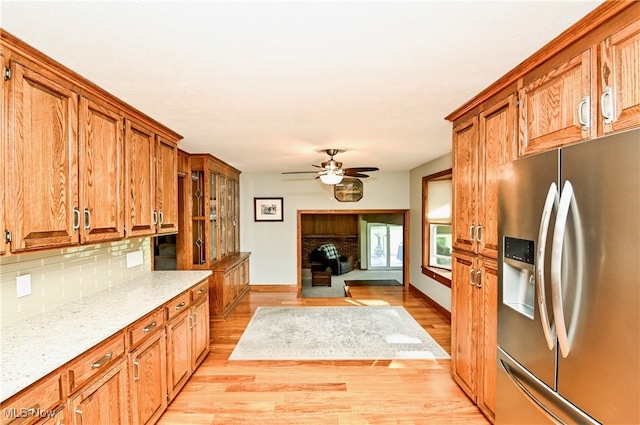 kitchen with light stone counters, ceiling fan, light hardwood / wood-style floors, stainless steel refrigerator with ice dispenser, and backsplash