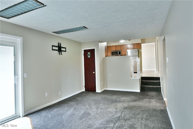 unfurnished living room with dark colored carpet and a textured ceiling