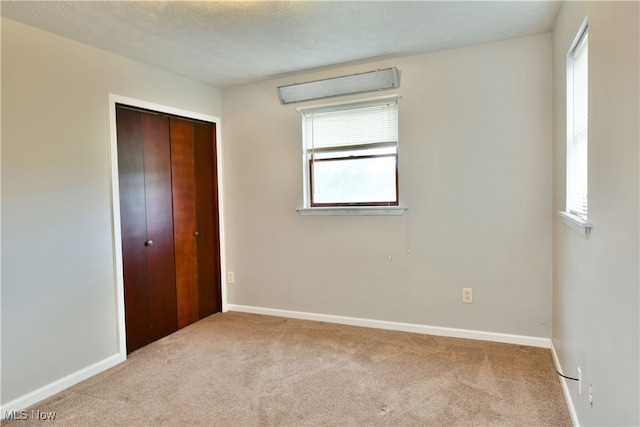 unfurnished bedroom with a closet, light colored carpet, and a textured ceiling