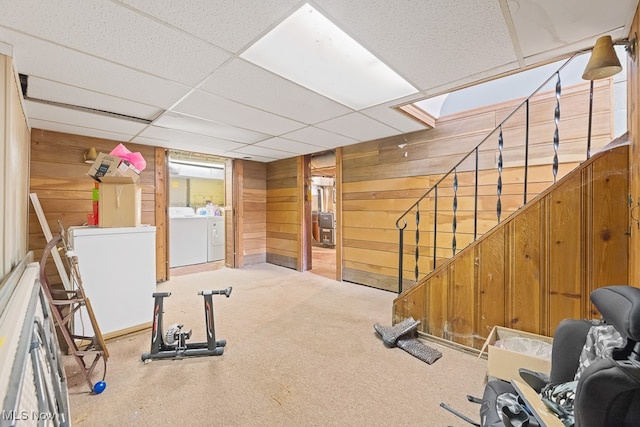 exercise area featuring a paneled ceiling, wood walls, separate washer and dryer, and light colored carpet