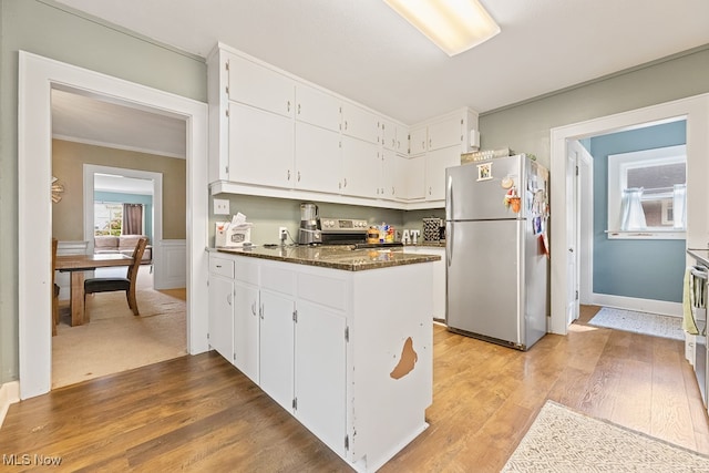 kitchen with wood-type flooring, dark stone counters, stainless steel fridge, and white cabinetry