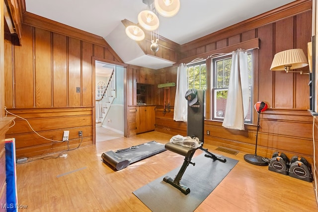 workout area with wooden walls, lofted ceiling, and light hardwood / wood-style floors