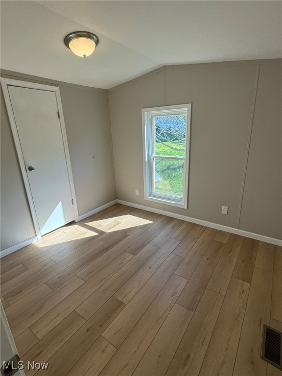 spare room with lofted ceiling and light wood-type flooring