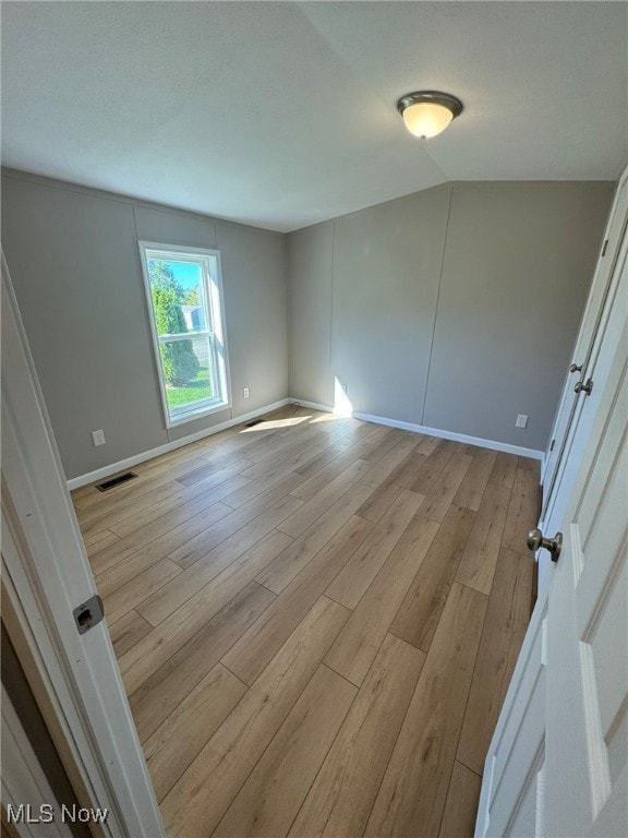 spare room with light hardwood / wood-style flooring and lofted ceiling