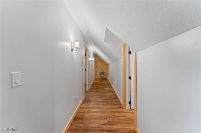 hall with vaulted ceiling, hardwood / wood-style flooring, and a textured ceiling