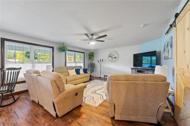 living room with wooden walls, ceiling fan, dark wood-type flooring, a barn door, and a textured ceiling