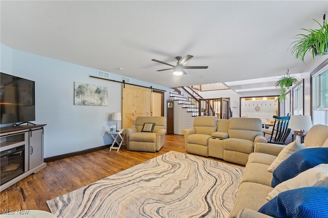 living room with a barn door, wood-type flooring, and ceiling fan