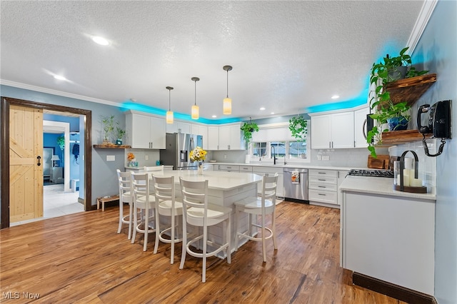 kitchen with appliances with stainless steel finishes, hanging light fixtures, white cabinetry, and light hardwood / wood-style flooring