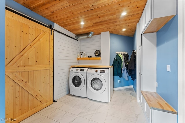 clothes washing area with washing machine and dryer, a barn door, wooden ceiling, and cabinets