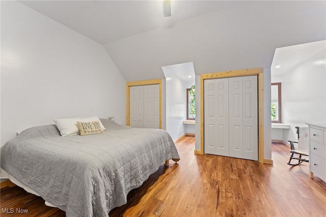 bedroom featuring lofted ceiling, light wood-type flooring, multiple closets, and multiple windows