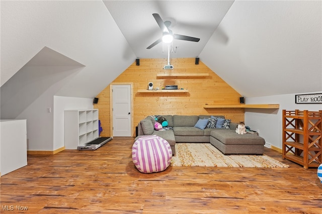 living room featuring lofted ceiling, wood-type flooring, wood walls, and ceiling fan