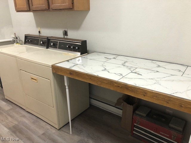 washroom featuring cabinets, light wood-type flooring, baseboard heating, and washing machine and clothes dryer