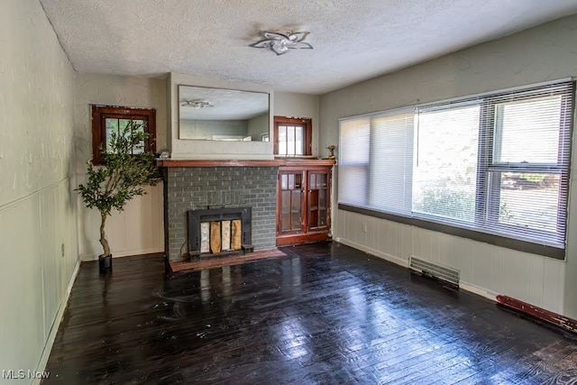 living room featuring a brick fireplace, dark hardwood / wood-style floors, a textured ceiling, and a healthy amount of sunlight