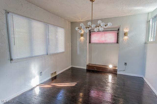 spare room featuring dark wood-type flooring and a chandelier