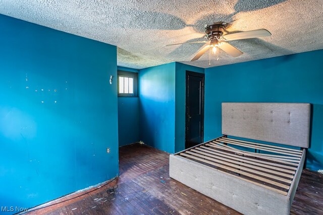 unfurnished bedroom with ceiling fan, a textured ceiling, and dark wood-type flooring