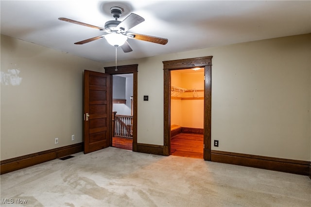 unfurnished bedroom featuring light carpet, ceiling fan, a closet, and a walk in closet