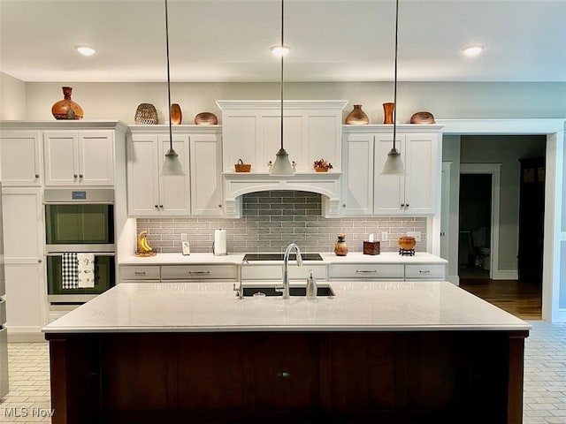 kitchen featuring a center island with sink, light stone counters, and hanging light fixtures