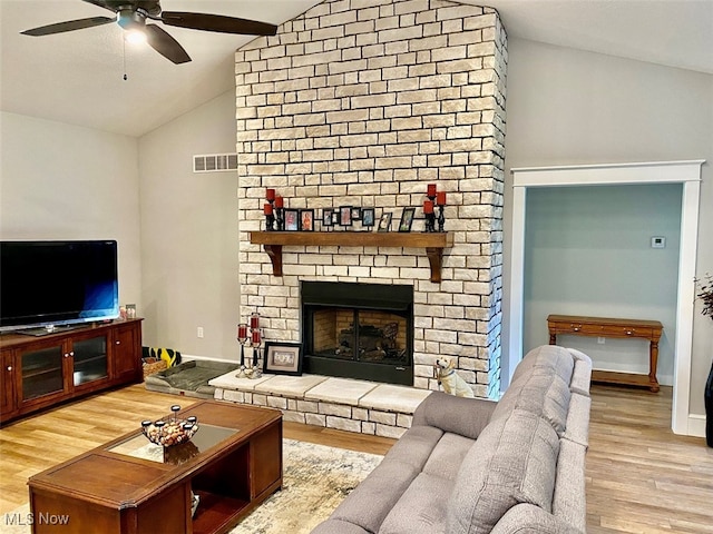 living room with ceiling fan, a stone fireplace, vaulted ceiling, and light hardwood / wood-style flooring