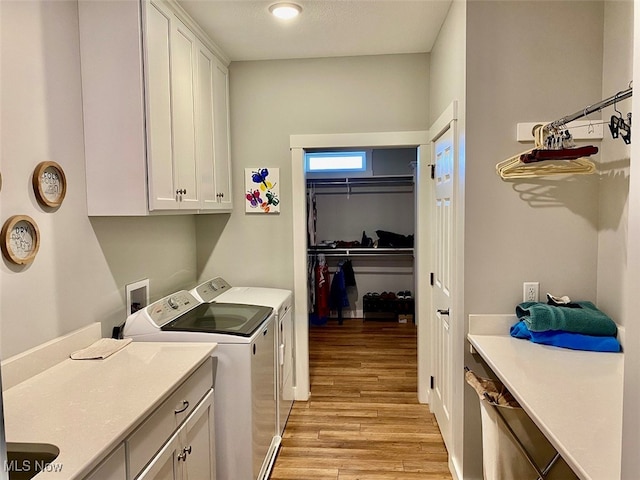 laundry room featuring a textured ceiling, cabinets, light wood-type flooring, and washer and clothes dryer