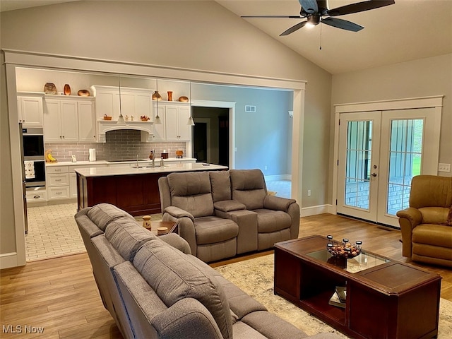 living room featuring ceiling fan, sink, french doors, light hardwood / wood-style flooring, and high vaulted ceiling