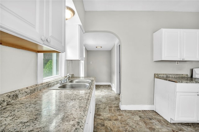 kitchen featuring light stone counters, white cabinetry, and sink