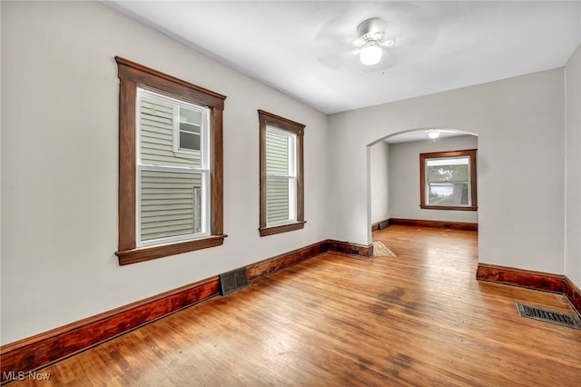 empty room with a healthy amount of sunlight, ceiling fan, and light hardwood / wood-style floors