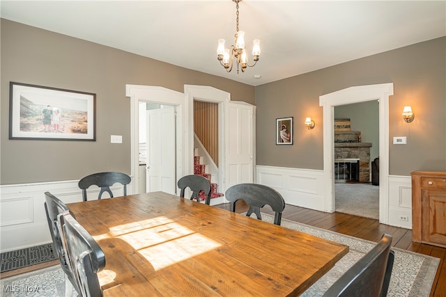 dining room with a stone fireplace, a chandelier, and dark hardwood / wood-style flooring