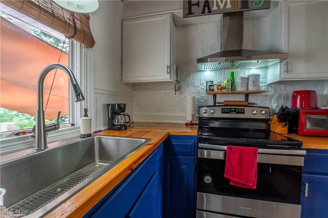 kitchen with wall chimney exhaust hood, sink, stainless steel electric range oven, butcher block countertops, and white cabinetry