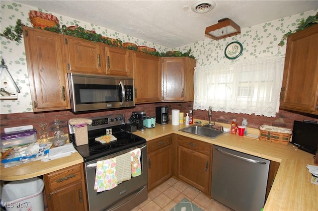 kitchen featuring stainless steel appliances, a sink, visible vents, light countertops, and wallpapered walls