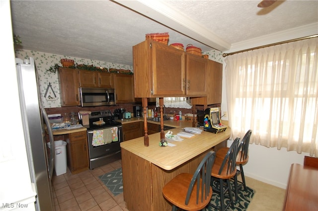 kitchen with a kitchen breakfast bar, stainless steel appliances, kitchen peninsula, light tile patterned floors, and a textured ceiling