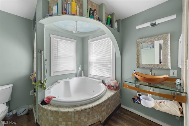 bathroom featuring vanity, tiled bath, hardwood / wood-style flooring, and toilet