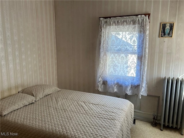 bedroom featuring radiator, light colored carpet, and wood walls